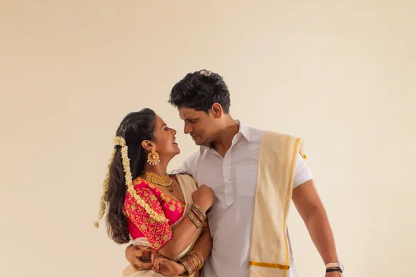 Kerala couple in traditional kasavu — bride in a set-saree with jasmine, groom in a mundu